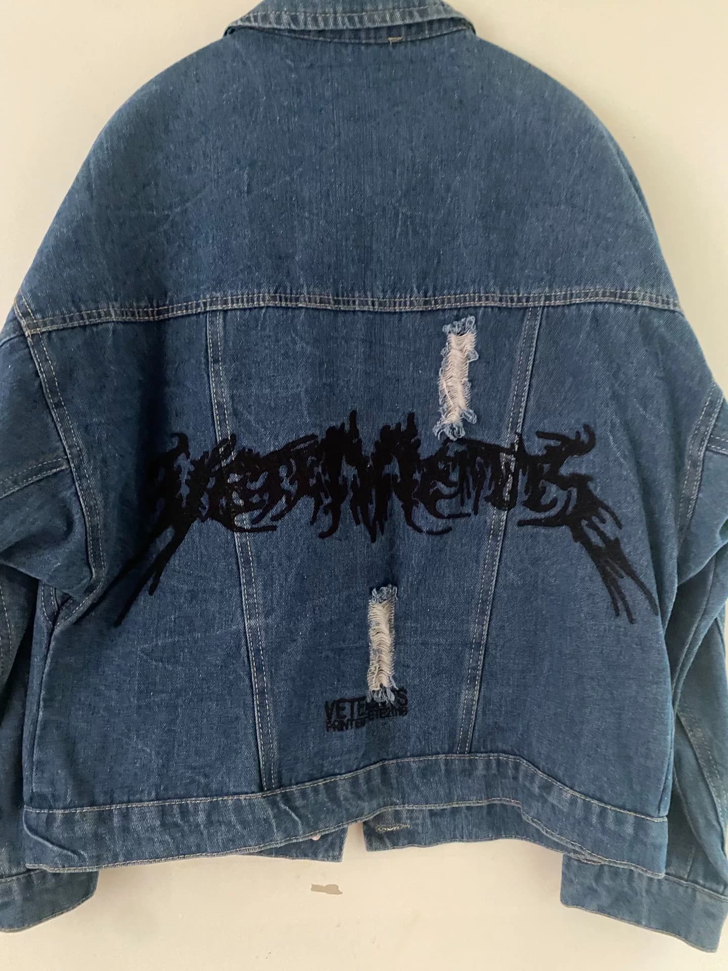 Из джинсовой куртки VETEMENTS с черной буквенной вышивкой на спине, груди